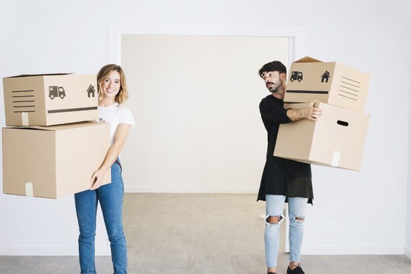 Man and woman smiling while holding cardboard boxes.
