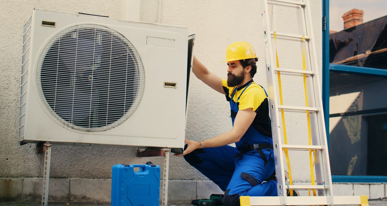 Professional worker starting work on malfunctioning air conditioner, using power drill to take apart condenser side coil panel. Capable electrician dismantling hvac system to check for faulty wires
